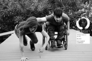 Μία κοπέλα με μακριά μαλλιά και τατουάζ στο δεξί της χέρι αναρριχάται σε μια ξύλινη ράμπα ενώ δίπλα της ένας νέος σε αναπηρικό αμαξίδιο πιάνεται με το ένα χέρι τεντωμένο από την ράχη της και ανεβαίνει δίπλα της.