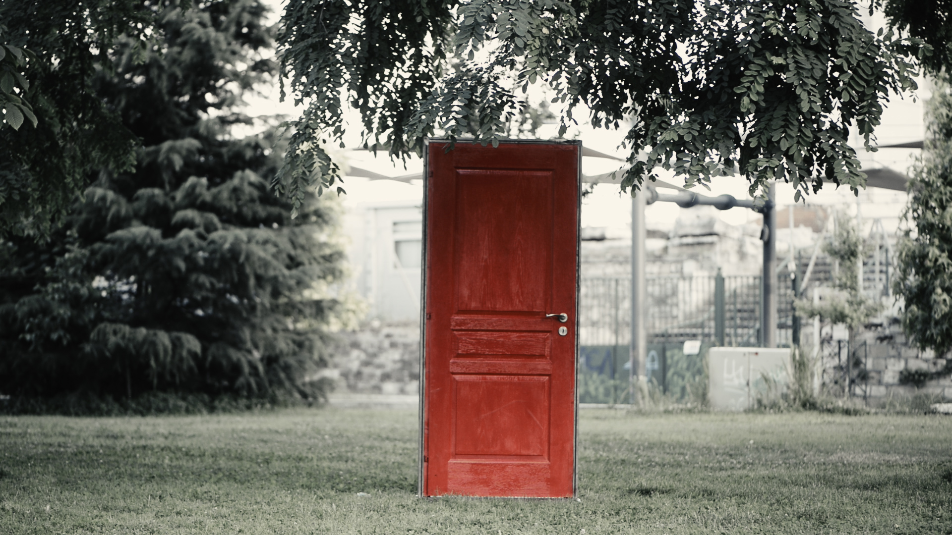 Αφίσα της ταινίας ΕΚΤΟΣ: Μία κατακόκκινη ξύλινη πόρτα στέκεται με το πλαίσιο της μόνο στo κέντρο ενός δημόσιου κήπου με χορτάρι και φυλλώδη δέντρα.