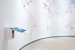 Σε έναν κυκλικό ψηλό τοίχο του Μουσείου εμφανίζεται ο Παγκόσμιος Χάρτης με κόκκινες βούλες σε διάφορα σημεία της Γης. Κλωστές ενώνουν τα σημεία μεταξύ τους δημιουργώντας έναν ιστό. Στα αριστερά της αίθουσας, ένα αντίγραφο του χάρτη σε μικρότερο μέγεθος με ανάγλυφα στοιχεία και λεζάντες σε braille δίνει τη δυνατότητα στους επισκέπτες με οπτική αναπηρία να αγγίξουν το έκθεμα και να κατανοήσουν το περιεχόμενό του.