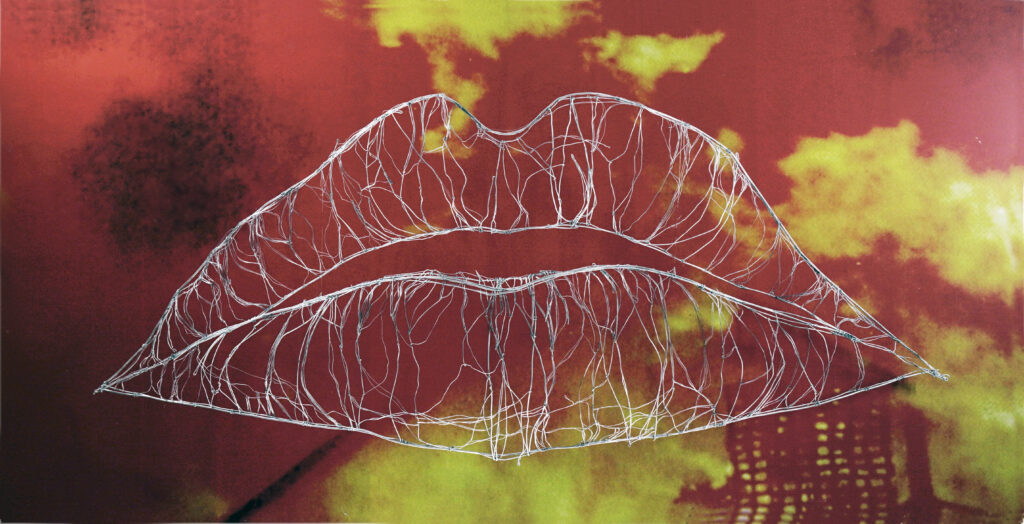 Art installation from the exhibition "Women's Issues". A huge structure made of thin wire forms two half-open lips. Behind them a photo of burning buildings processed gives the lips in front a fire-red tint.