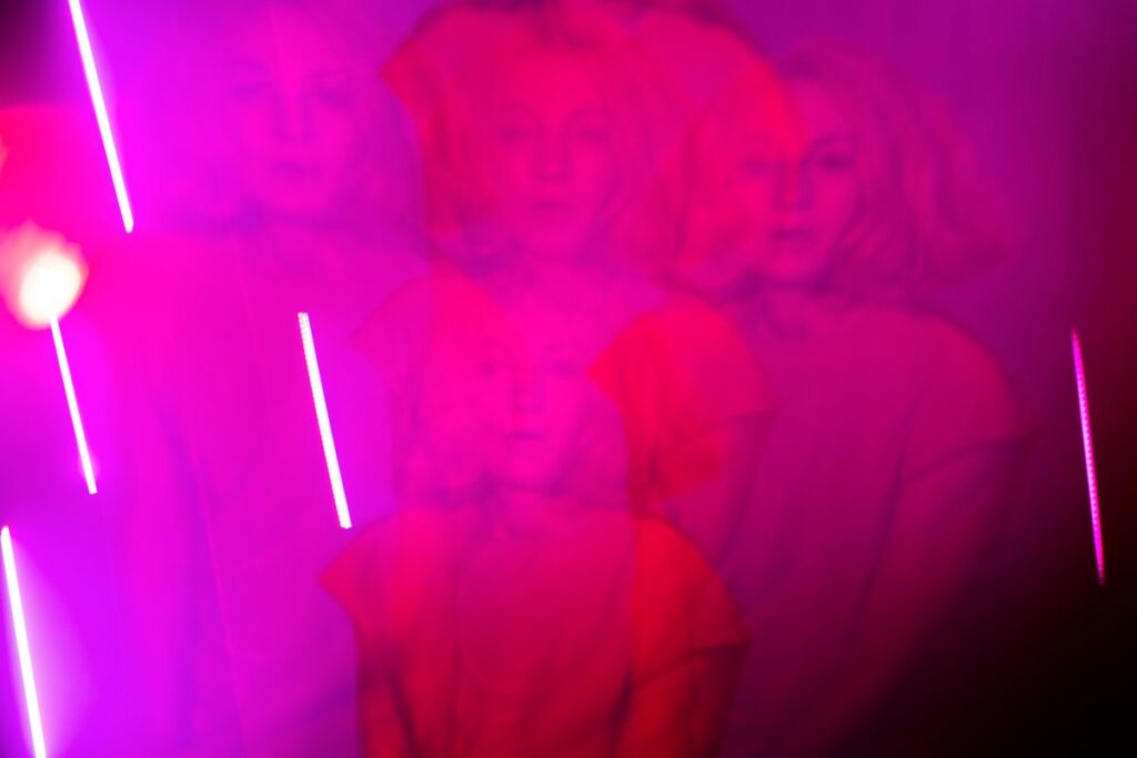 The photograph of a woman with blonde hair framed in several copies that partially overlap each other creates multiple portraits that, combined with the intense fuchsia lighting and the blurred quality of the final image, looks like a piece of a dream fantasy.