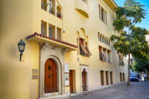 Εξωτερική όψη του Μουσείου "Αγγελική Χατζημιχάλη" σε πλακόστρωτο δρομάκι της Πλάκας. Το κτίσμα, δημιούργημα του αρχιτέκτονα Αριστοτέλη Ζάχου, είναι δίπατο σε κιτρινωπή απόχρωση και διακρίνεται για την ιδιαίτερη αρχιτεκτονική που συνδυάζει παραδοσιακά στοιχεία που βρίσκουμε στη μακεδονίτικη αρχιτεκτονική και στη νεοβυζαντινή παράδοση όπως τα ξύλινα κουφώματα, τα σκαλιστά πλαίσια γύρω από τα παράθυρα ή τις πόρτες και τη σκεπή από κεραμίδια.