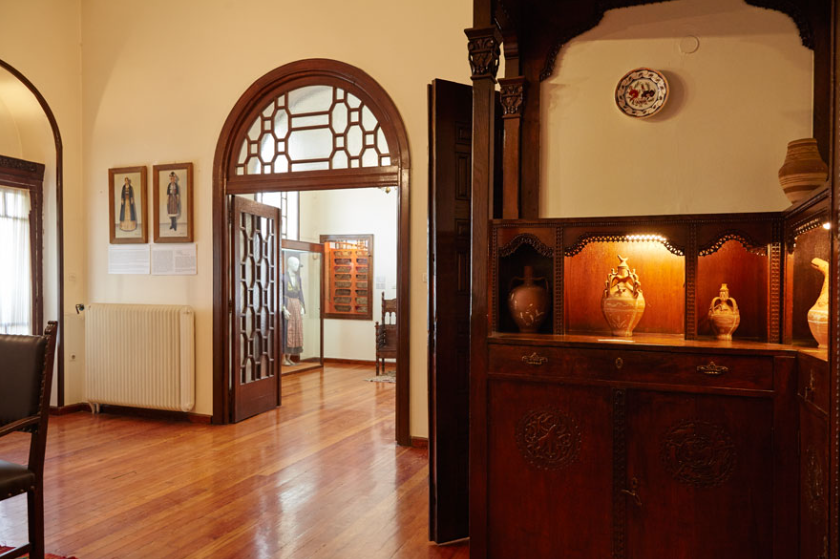 View from the interior of the museum with a carved wooden shelf on which ceramic carved vases of various sizes are placed. In the background is a large double door with an arch made of wood and glass.