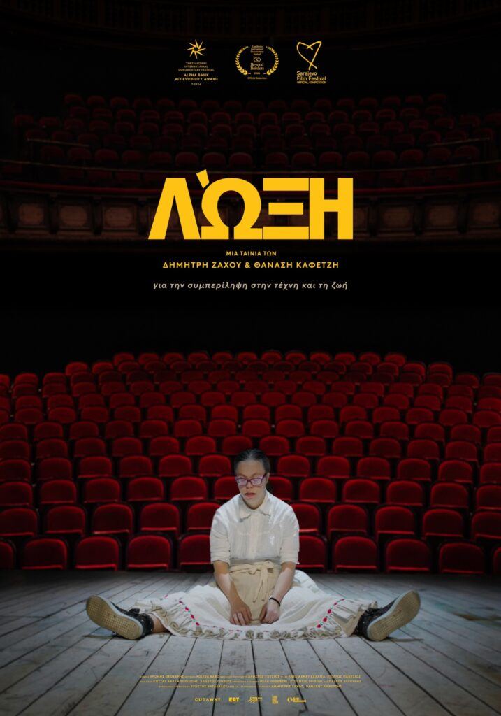 Poster of the film "Loxy". On an empty stage with wooden planks sits a young woman in a white shirt and a white skirt. She has her legs open and her hands resting on her apron. She has a round face and pronounced lips. She wears purple eyeglasses. She is a person with down syndrome. Behind her spread the empty red velvet theatre seats. At the top of the poster in yellow bold letters is the title and underneath is written "a film by Dimitris Zachos and Thanasis Kafetzis about inclusion in art and life.