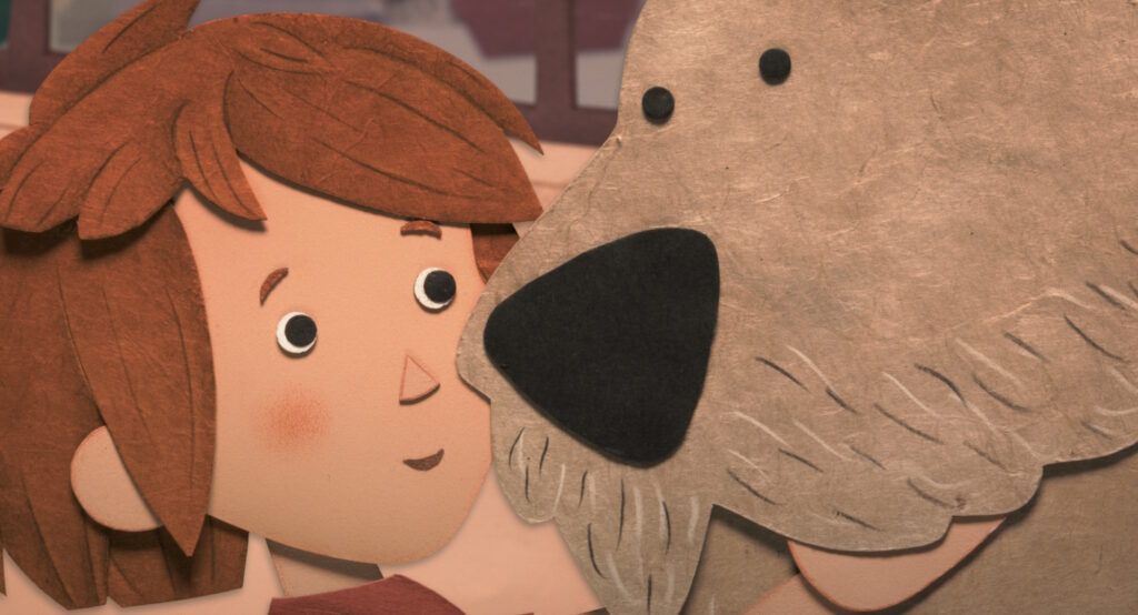 Απόσπασμα ταινίας από δισδιάστατες φιγούρες φτιαγμένες από τσόχα. Ένα μικρό αγόρι με πορτοκαλοκάστανα μαλλιά κολλά το πρόσωπό του στη μουσούδα ενός καφετί σκύλου.