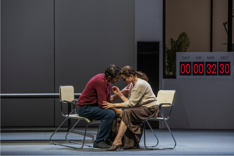 Σε έναν άδειο χώρο, ένα χρονόμετρο με κόκκινα ψηφία στο πίσω μέρος δεξιά, δείχνει 32 λεπτά και 30 δευτερόλεπτα. Μπροστά και στο κέντρο, ένας άνδρας και μια γυναίκα γύρω στα 45 κάθονται σε μεταλλικές καρέκλες αντικριστά με τα μέτωπά τους ενωμένα και τα χέρια τους να αγγίζονται σα να συζητούν κάτι ιδιωτικής φύσεως.
