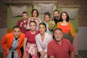 Με φόντο τρία κρεβάτια στημένα στον τοίχο σε όρθια θέση, οκτώ άτομα ποζάρουν στον φακό. Κάποιοι μοιάζουν να φορούν πιτζάμες και ρόμπες, κάποιοι ιατρικές ρόμπες κι άλλοι απλά καθημερινά ρούχα σε απαλές αποχρώσεις.