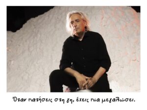 Ένας άνδρας με γκρίζα μαλλιά ως τους ώμους και μαύρα ρούχα κάθεται πάνω σε έναν τεράστιο ανάγλυφο λευκό όγκο που θυμίζει χιονοστιβάδα κοιτώντας σοβαρός προς την κάμερα. Με χειρόγραφους χαρακτήρες που θυμίζουν γράμματα παιδιού, στο κάτω μέρος γράφει: Όταν πατήσεις στη γη, έχεις πια μεγαλώσει.
