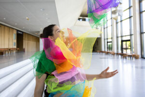 Στο απλόχωρο φουαγιέ του Μεγάρου Μουσικής Αθηνών μια νεαρή κοπέλα σε προφίλ κρύβεται σχεδόν ολόκληρη από πλήθος πολύχρωμων μαντηλιών που ίπτανται μπροστά της. Από το ελαφρώς υψωμένο αριστερό της χέρι σκορπίζει στον αέρα σαν ταχυδακτυλουργός ένα ακόμα μπουκετάκι μαντηλιών που πετά ανάλαφρα μπροστά στα μάτια της.