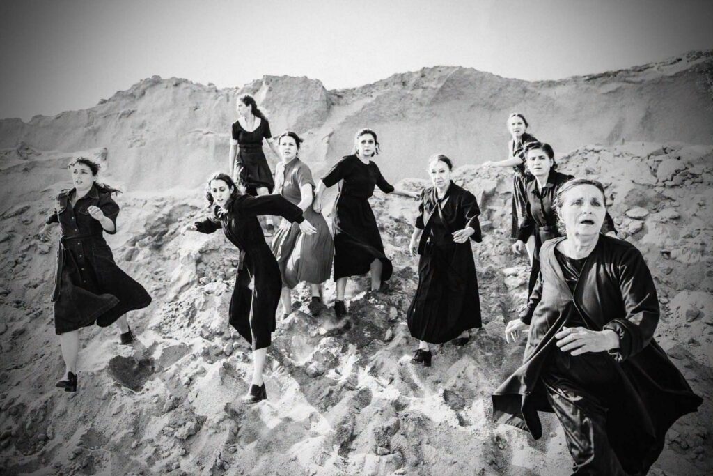Women dressed in black hurry down a rocky slope. They look ahead with weary faces and anxious gazes.