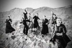 Μαυροφορεμένες γυναίκες κατεβαίνουν τρεχάτες ένα βραχώδες ύψωμα. Κοιτούν μπροστά με πρόσωπα ταλαιπωρημένα και βλέμματα ανήσυχα.