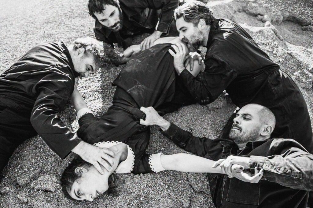 Four men are thrown over the body of a woman lying on the ground. They pull at her clothes, seize her by the neck and torso, and forcefully hold her legs. The woman’s gaze is turned upward, as if caught in a moment of crisis or already lifeless.