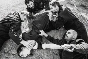 Τέσσερις άνδρες έχουν ριχτεί πάνω στο σώμα μιας γυναίκας πεσμένης στο χώμα. Την τραβούν από τα ρούχα, τη γραπώνουν από το λαιμό και το σώμα, τις κρατούν τα πόδια με δύναμη. Η γυναίκα έχει στραμμένο το βλέμμα ψηλά σα να βρίσκεται σε κάποια κρίση ή ακόμα και να έχει πεθάνει.